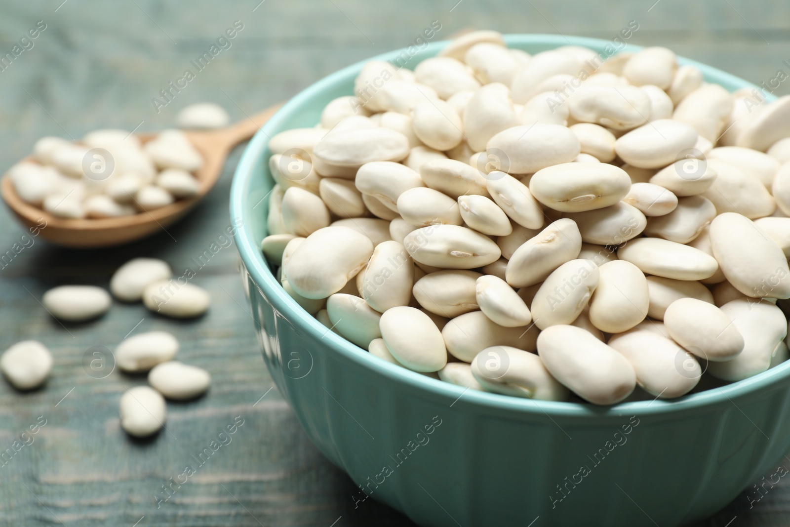 Photo of Bowl of uncooked white beans on blue wooden table, closeup