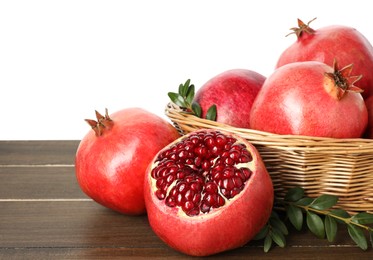 Photo of Fresh pomegranates in wicker basket and green leaves on wooden table against white background