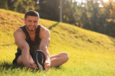 Photo of Attractive man doing exercises on green grass in park, space for text. Stretching outdoors