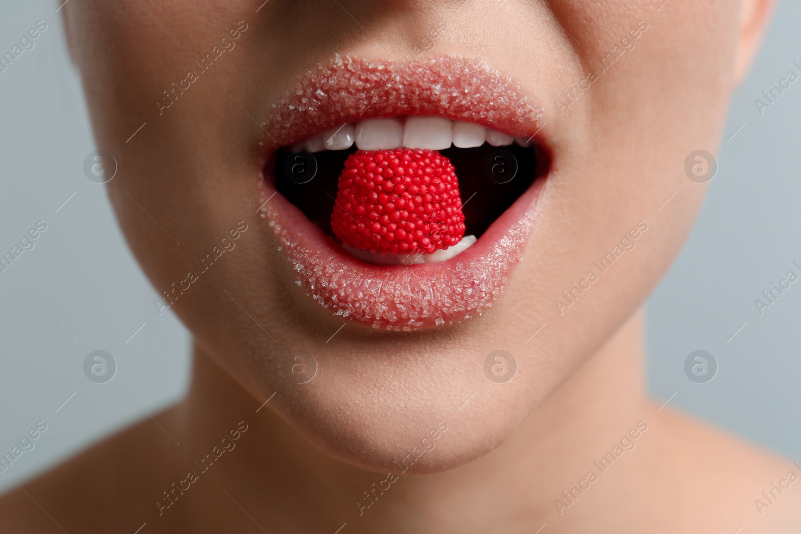 Photo of Woman with lips covered in sugar eating candy on light grey background, closeup