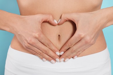 Photo of Woman making heart with hands on her belly against light blue background, closeup