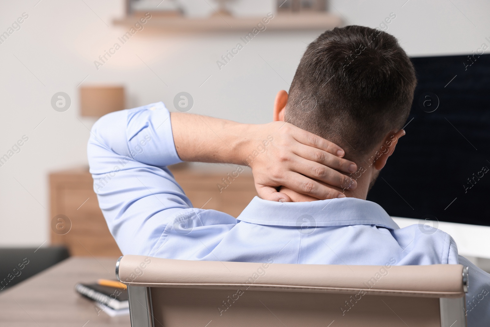 Photo of Man suffering from neck pain in office, back view