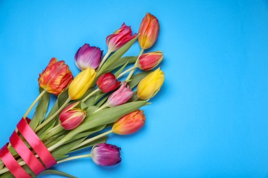 Photo of Bouquet of beautiful colorful tulip flowers tied with red ribbon on light blue background, top view. Space for text