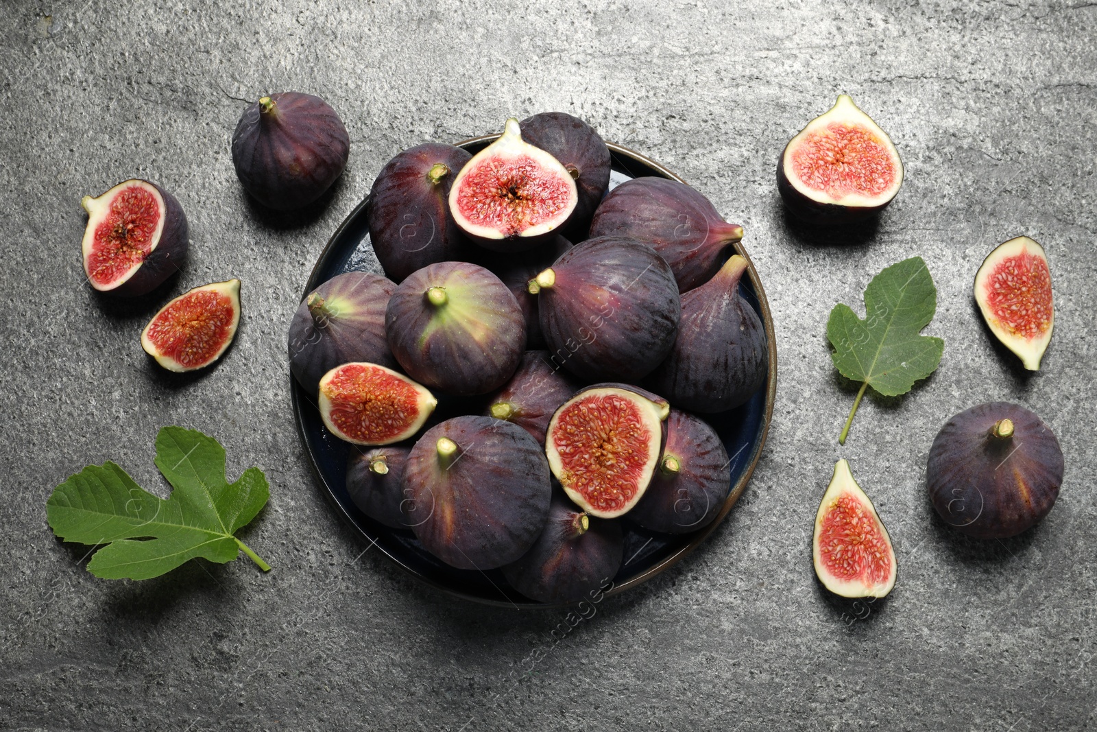 Photo of Whole and cut ripe figs with leaves on light grey textured table, flat lay