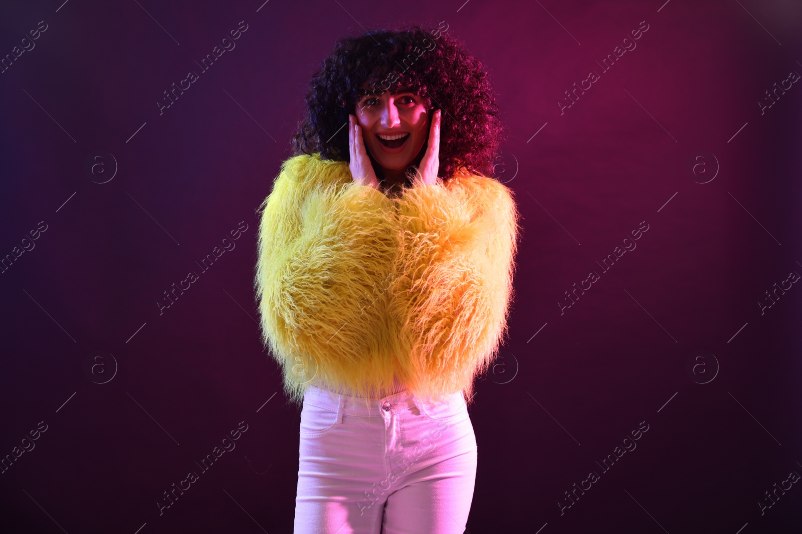 Photo of Beautiful young woman in yellow fur coat on color background in neon lights