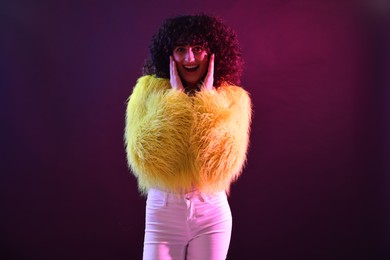 Photo of Beautiful young woman in yellow fur coat on color background in neon lights