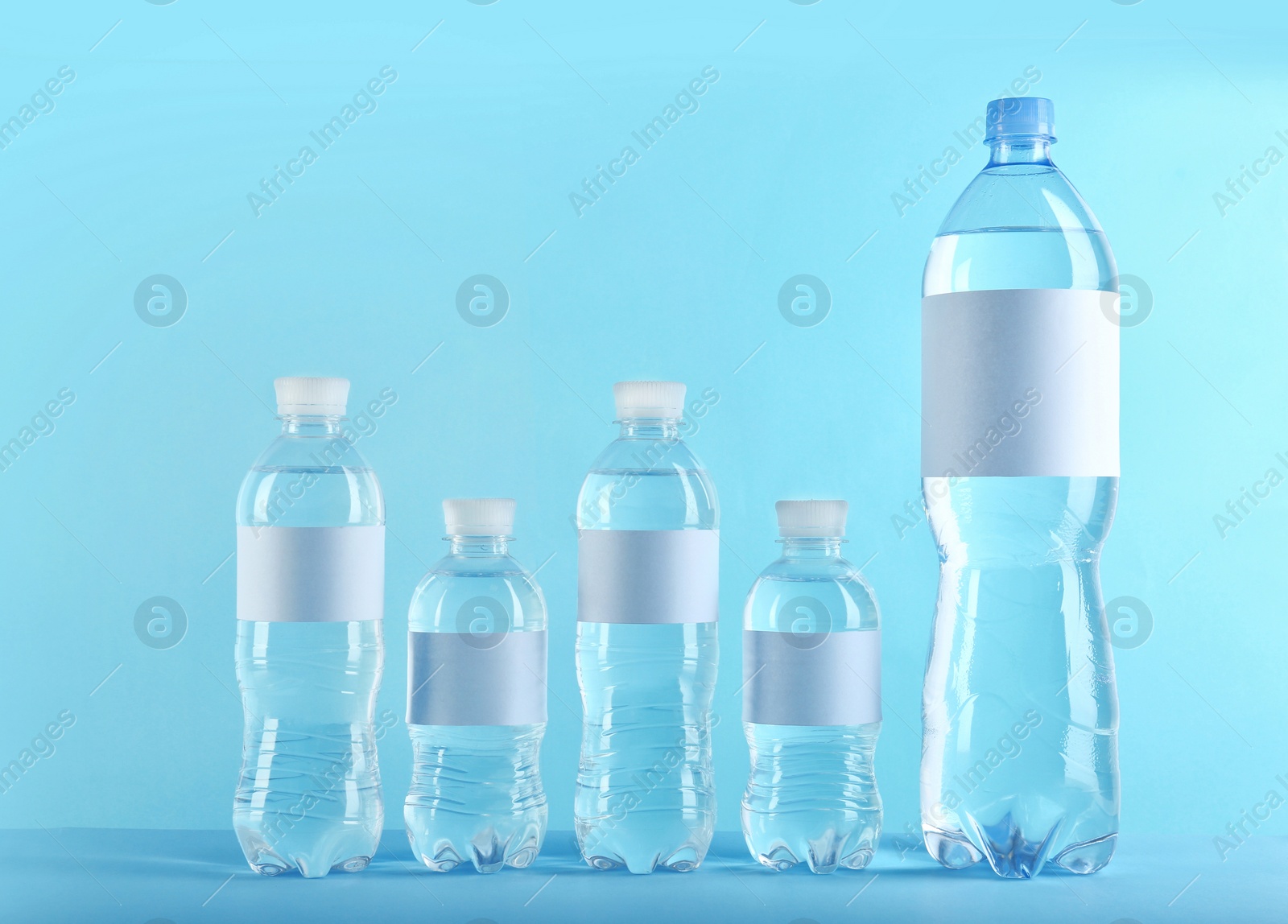 Photo of Different bottles of pure water with blank tags on color background