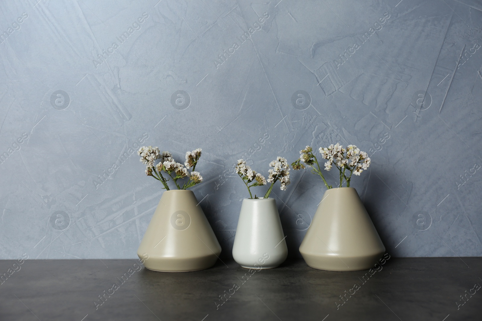 Photo of Beautiful ceramic vases with flowers on table against color wall. Space for text