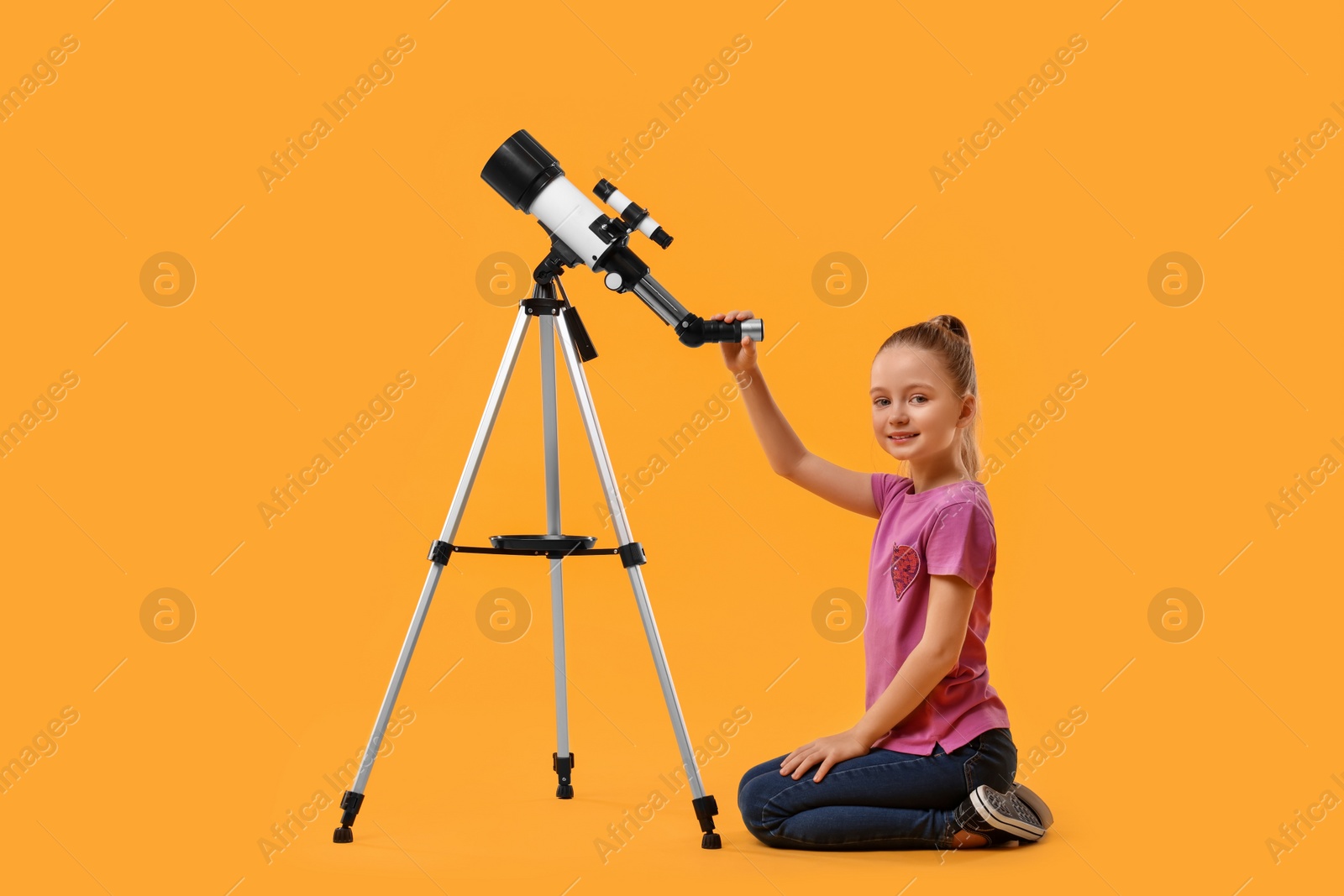 Photo of Happy little girl with telescope on orange background