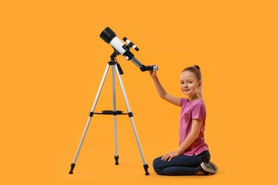 Photo of Happy little girl with telescope on orange background
