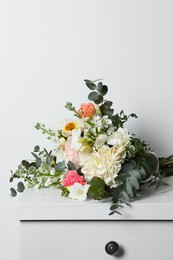 Bouquet with beautiful flowers on chest of drawers near white wall