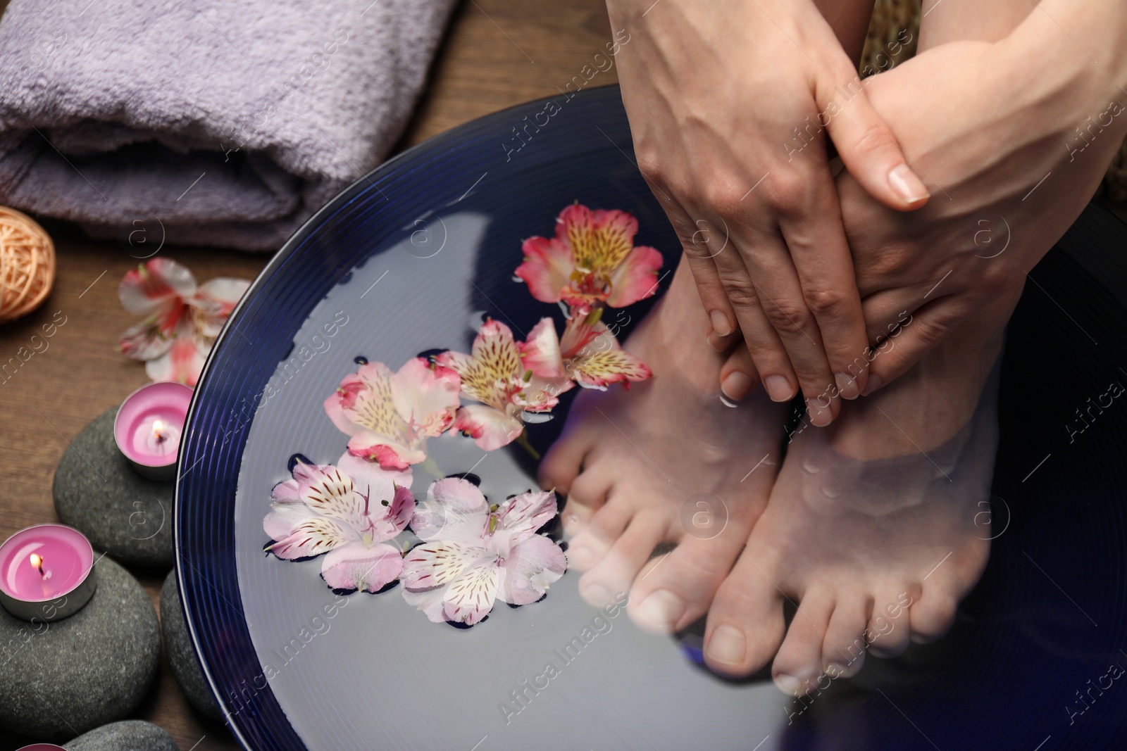 Photo of Woman soaking her feet in bowl with water and flowers on floor, closeup. Spa treatment