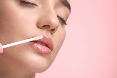 Photo of Woman applying lip gloss on pink background, closeup. Space for text