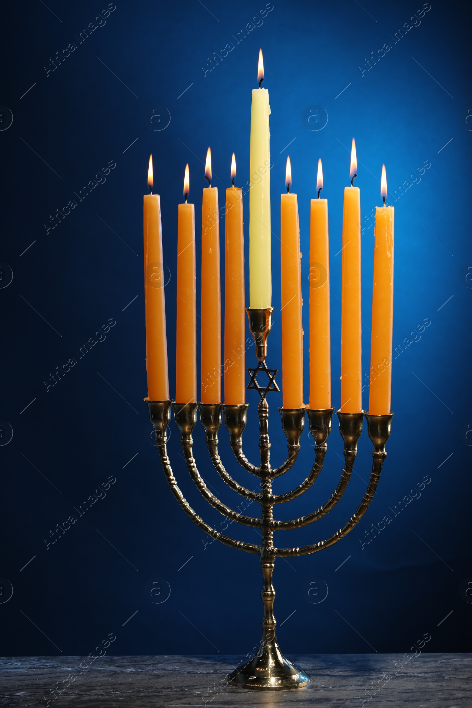 Photo of Hanukkah celebration. Menorah with burning candles on table against blue background