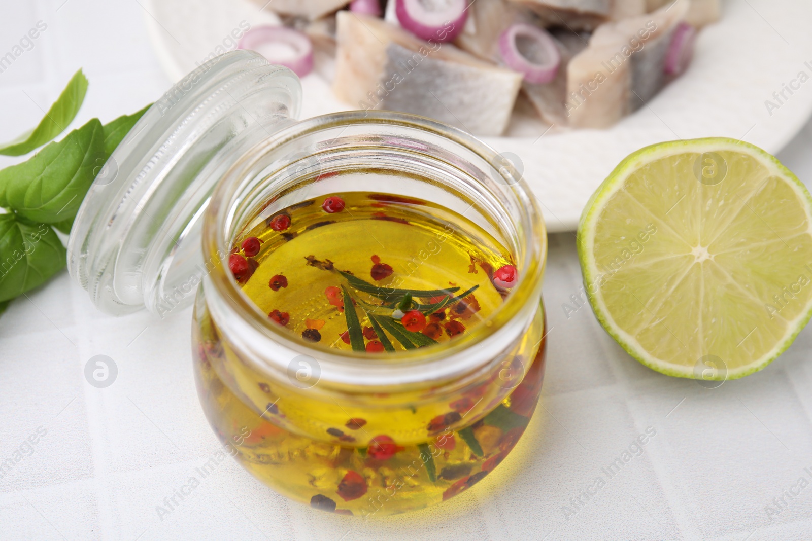 Photo of Tasty fish marinade in jar and lime on light tiled table, closeup