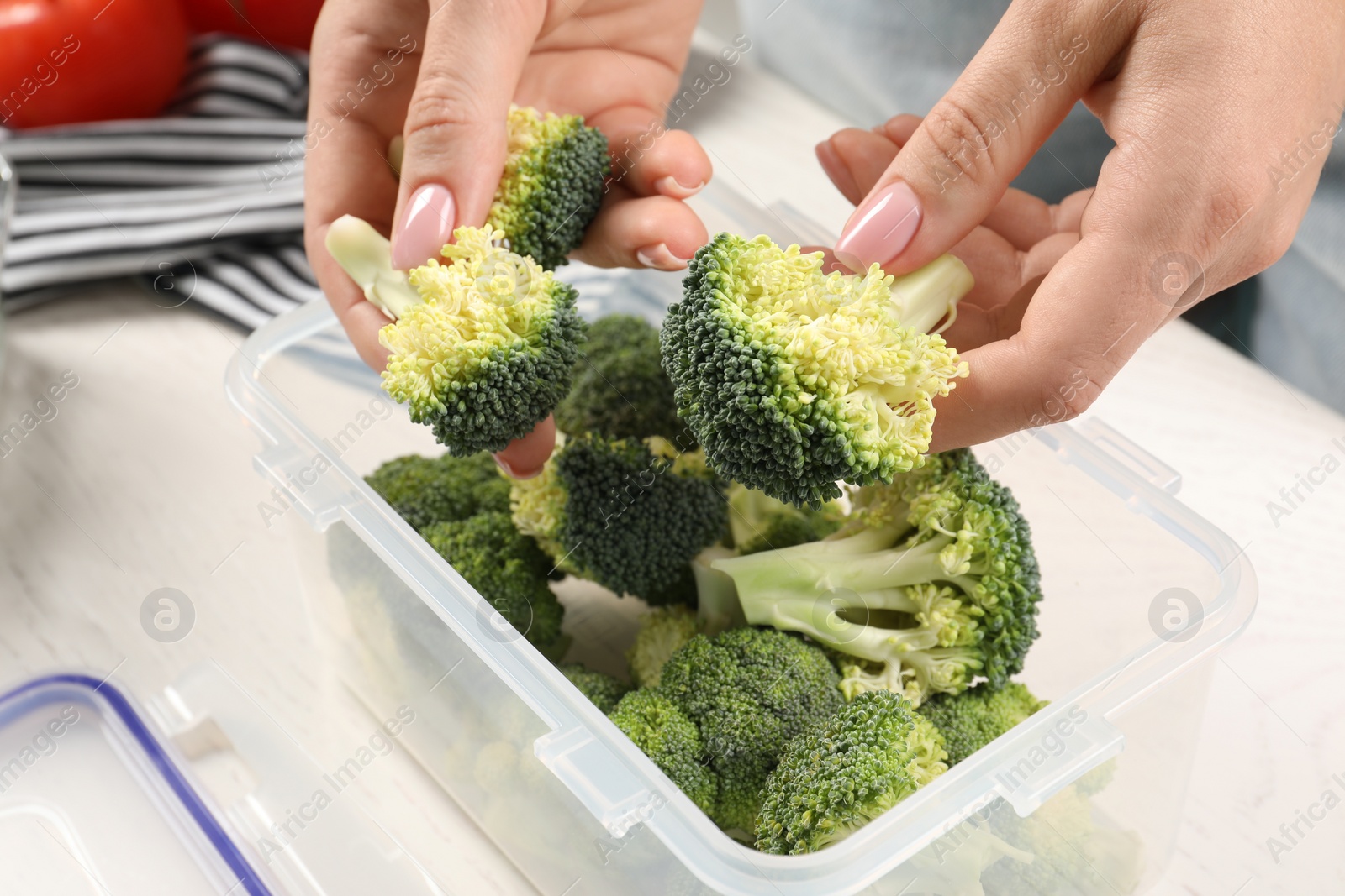 Photo of Woman putting broccoli into plastic container at white table, closeup. Food storage