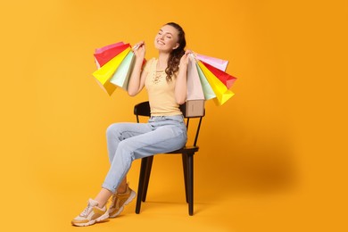 Photo of Happy woman holding colorful shopping bags on chair against orange background