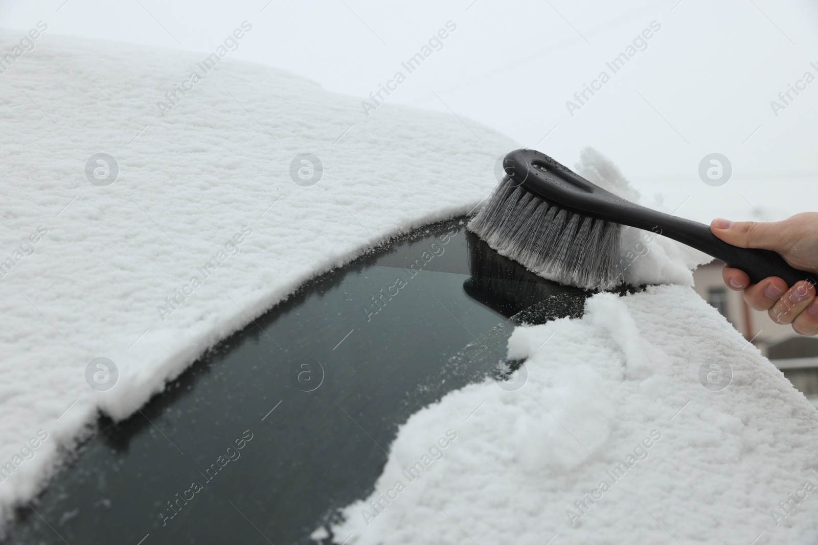 Photo of Woman cleaning car windshield from snow with brush, closeup