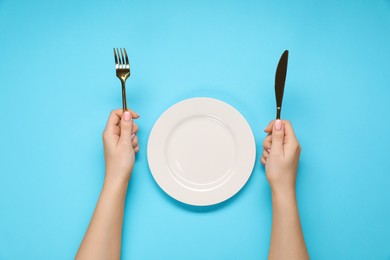 Photo of Woman holding fork and knife near empty plate at light blue table, top view