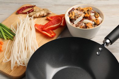 Black wok and products on light wooden table, closeup