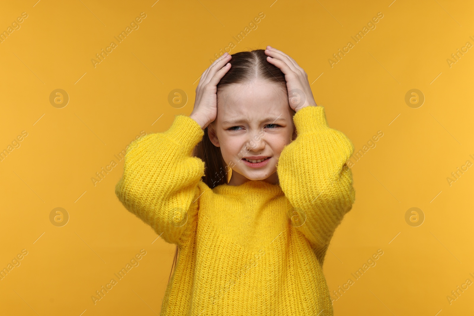 Photo of Little girl suffering from headache on yellow background