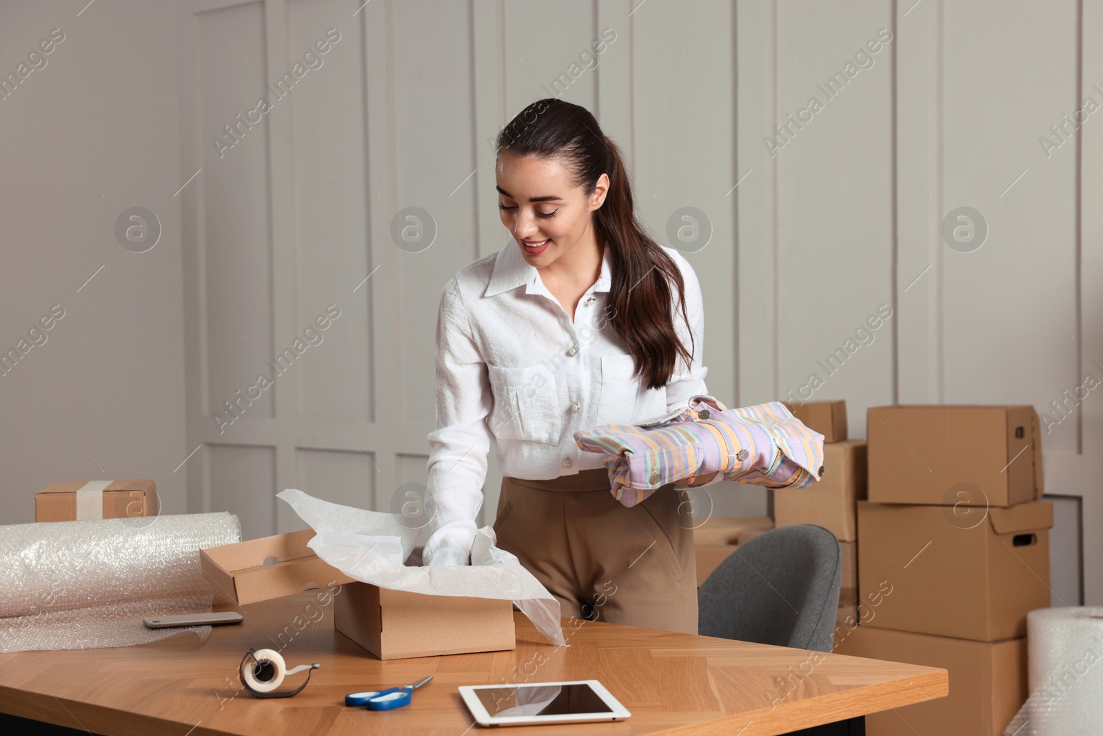 Photo of Seller packing clothes into cardboard box at table in office. Online store