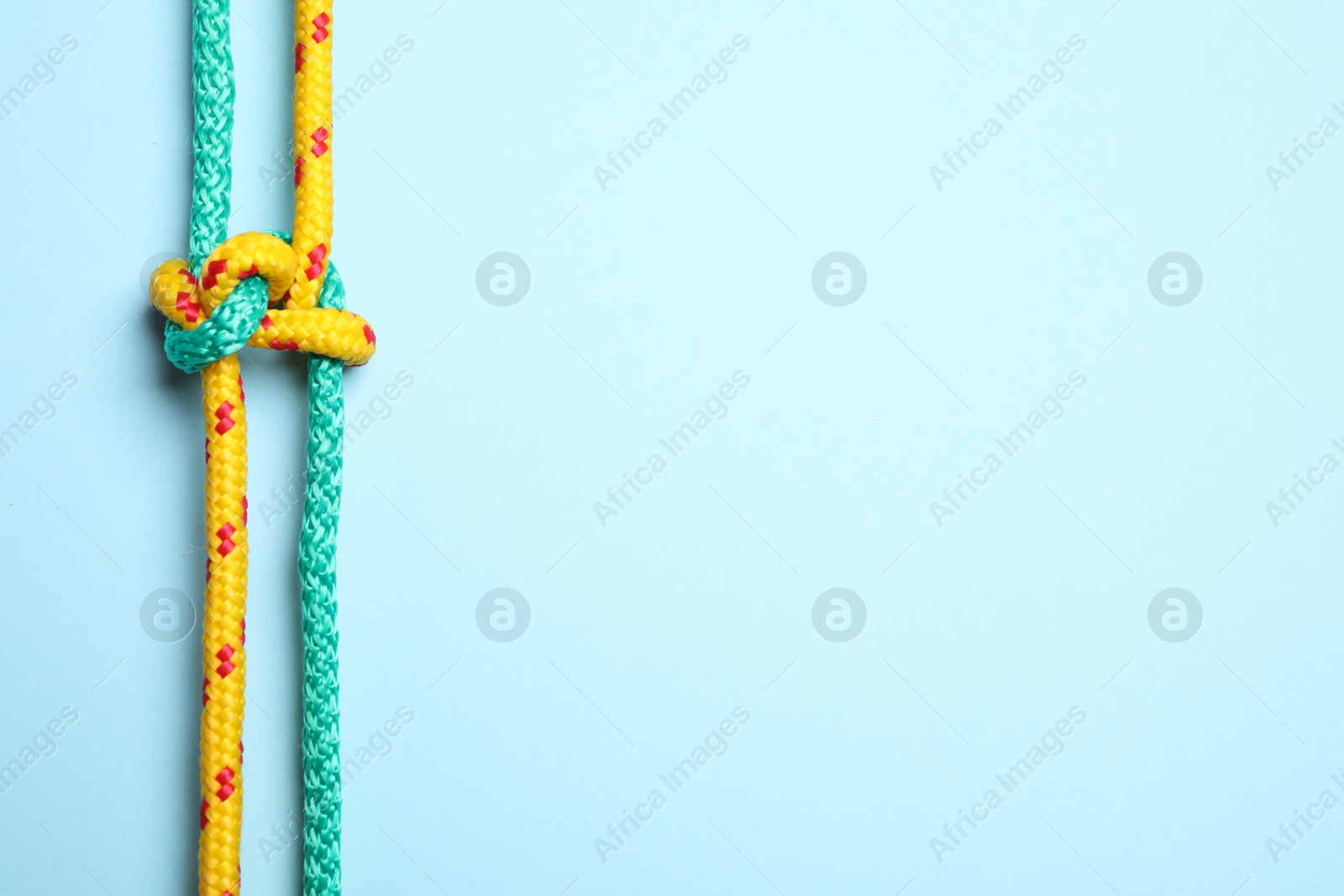 Photo of Top view of colorful ropes tied with knot on light blue background, space for text. Unity concept