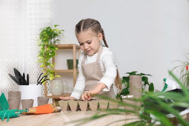 Photo of Little girl planting vegetable seeds into peat pots with soil at wooden table in room