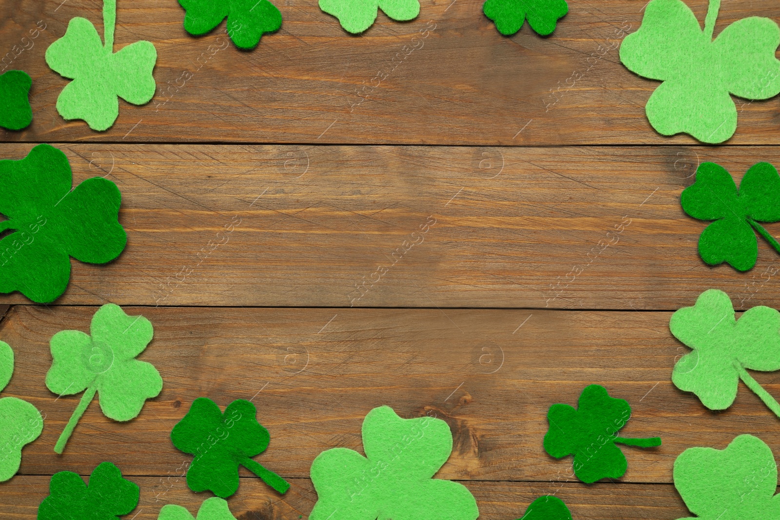 Photo of Frame made of decorative clover leaves on wooden table, flat lay with space for text. Saint Patrick's Day celebration