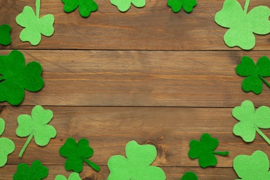 Frame made of decorative clover leaves on wooden table, flat lay with space for text. Saint Patrick's Day celebration