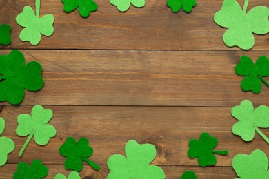 Photo of Frame made of decorative clover leaves on wooden table, flat lay with space for text. Saint Patrick's Day celebration