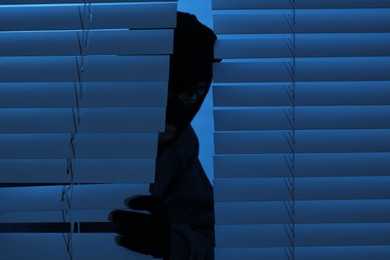 Photo of Thief looking out of blinds at night. Burglary