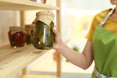 Photo of Woman putting jar of pickles on shelf indoors, closeup