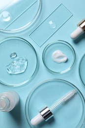 Photo of Petri dishes with samples of cosmetic serums, bottle and pipette on light blue background, flat lay