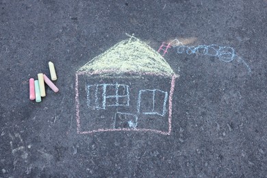 Photo of Child's house drawing and pieces of color chalk on asphalt, flat lay