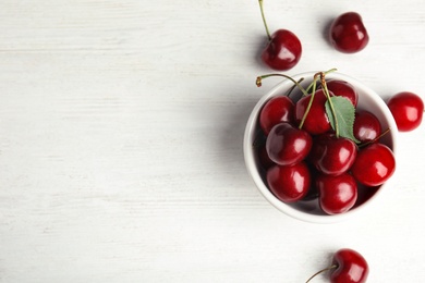 Photo of Bowl with sweet cherries on white wooden table, top view. Space for text