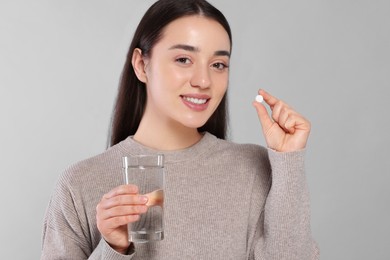 Happy woman with glass of water and pill on gray background