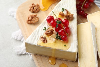 Photo of Brie cheese served with red currants, walnuts and honey on light table, closeup