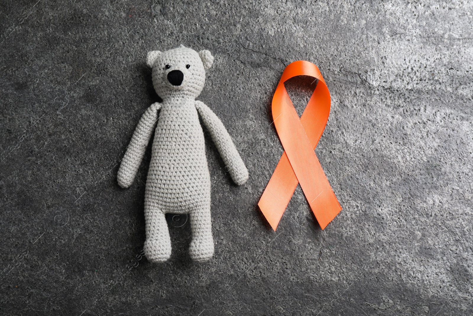 Photo of Orange ribbon and toy bear on grey table, flat lay. Multiple sclerosis awareness