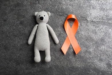 Orange ribbon and toy bear on grey table, flat lay. Multiple sclerosis awareness