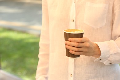 Woman holding takeaway paper cup outdoors, closeup and space for text. Coffee to go