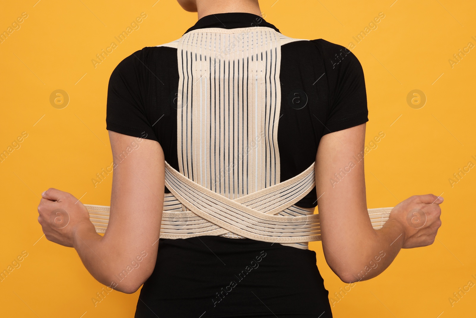 Photo of Closeup of woman with orthopedic corset on orange background, back view