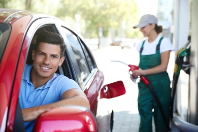 Photo of Man sitting in car while young worker refueling his auto at modern gas station