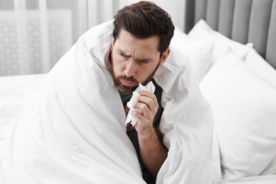 Photo of Sick man with tissue coughing on bed at home. Cold symptoms