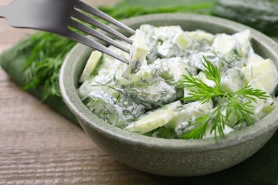 Photo of Eating delicious cucumber salad at wooden table, closeup