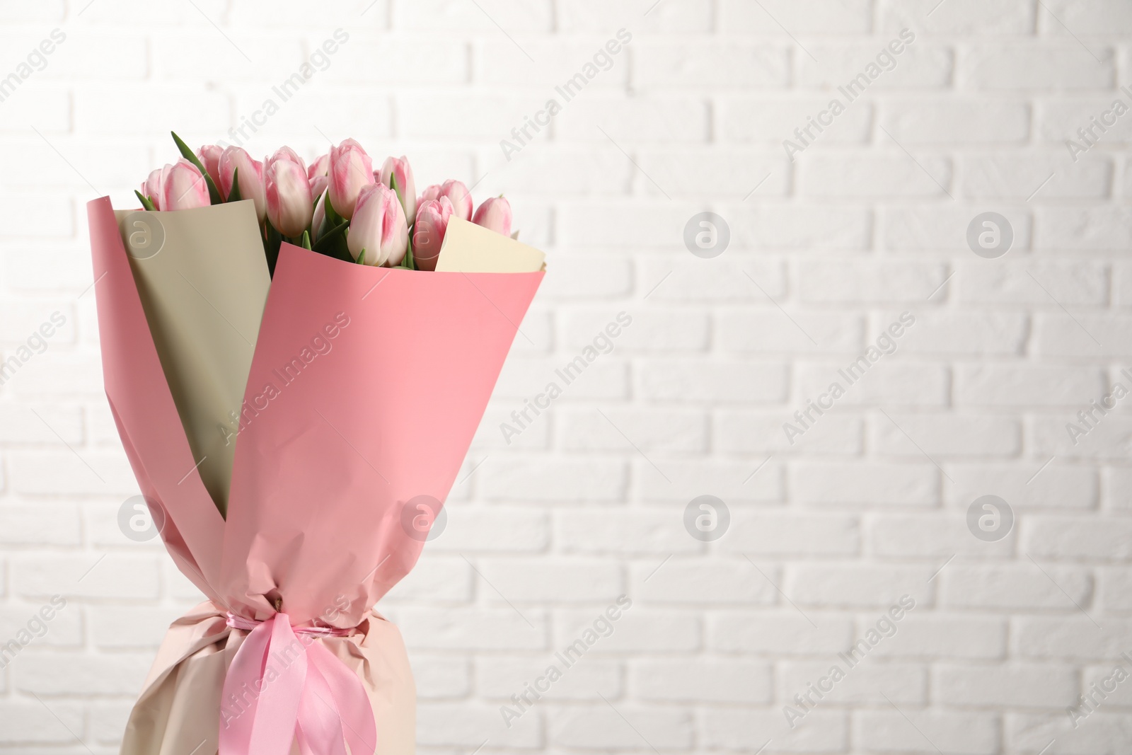 Photo of Beautiful bouquet of fresh pink tulips against white brick wall. Space for text