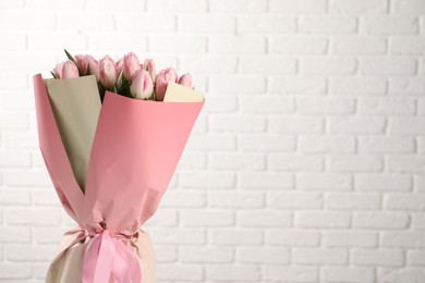 Photo of Beautiful bouquet of fresh pink tulips against white brick wall. Space for text