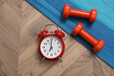 Photo of Alarm clock, yoga mat and dumbbells on wooden background, flat lay. Morning exercise