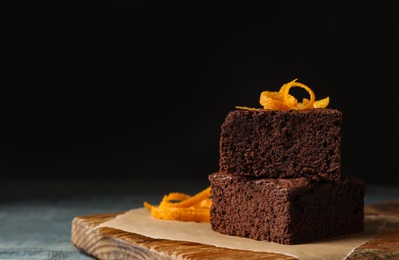 Fresh brownies decorated with orange peel on wooden board, space for text. Delicious chocolate pie