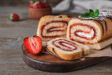 Tasty cake roll with strawberry jam and cream on wooden table